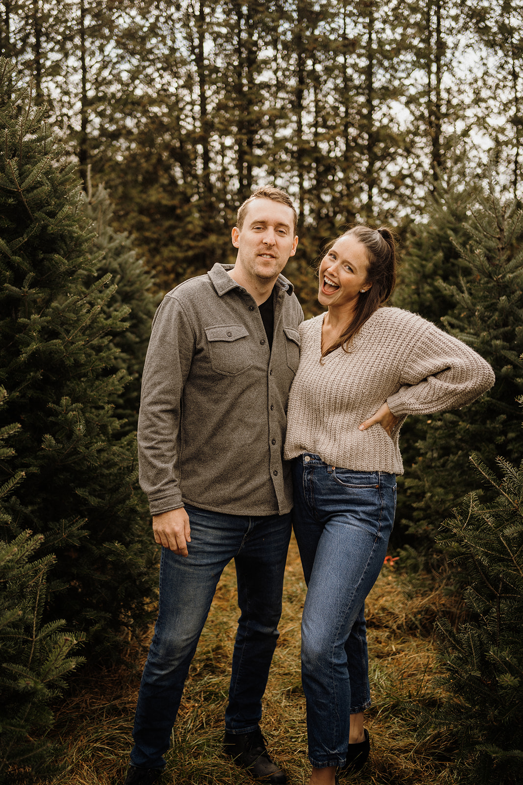 A husband and wife standing between Christmas Trees.