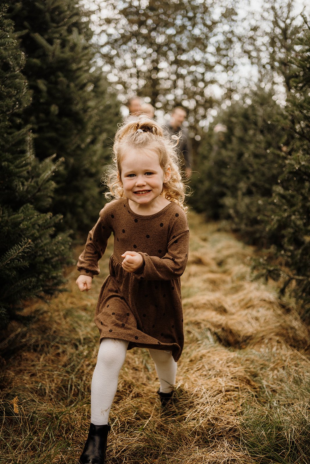 A little girl running outside between Christmas Trees.