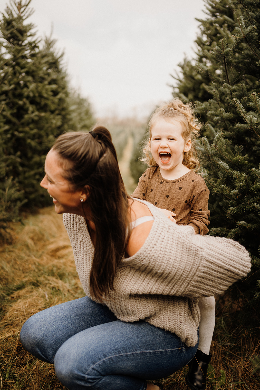 A mother and her daughter outside between Christmas Trees.