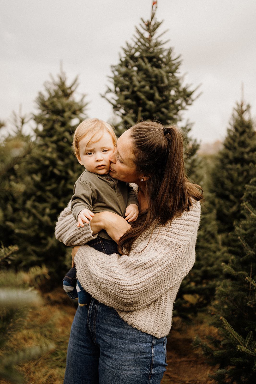 A mother and with her son in her arms between Christmas Trees.