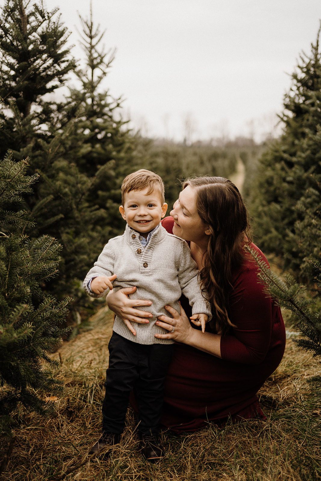 A mother and son sitting beside Christmas Trees.