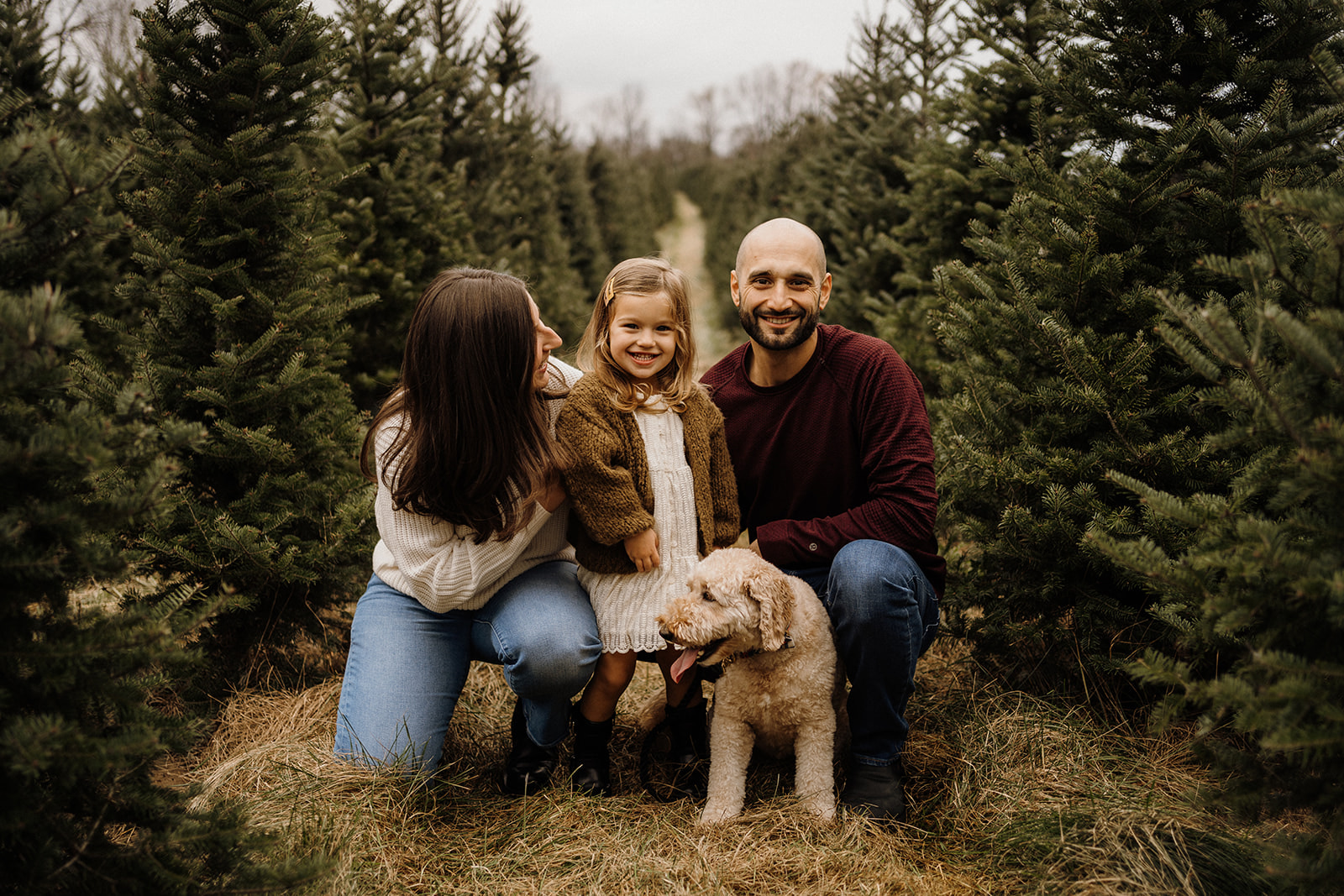 A family of four outside beside the Christmas Trees.