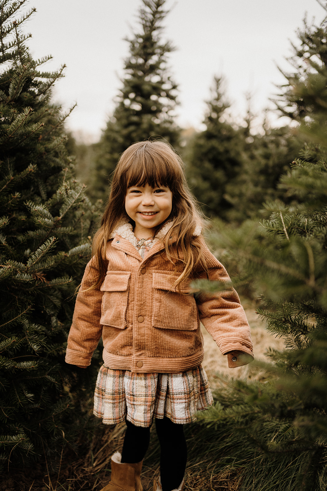 A child standing outside in front of Christmas Trees.