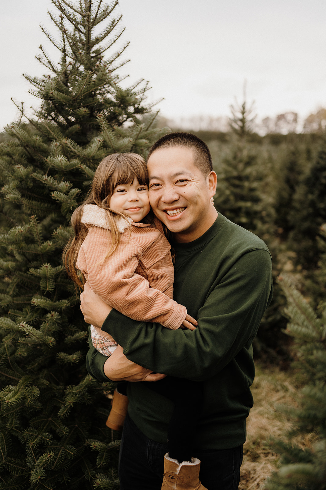 A man holding his child in his arms outside in front of a Christmas Tree.