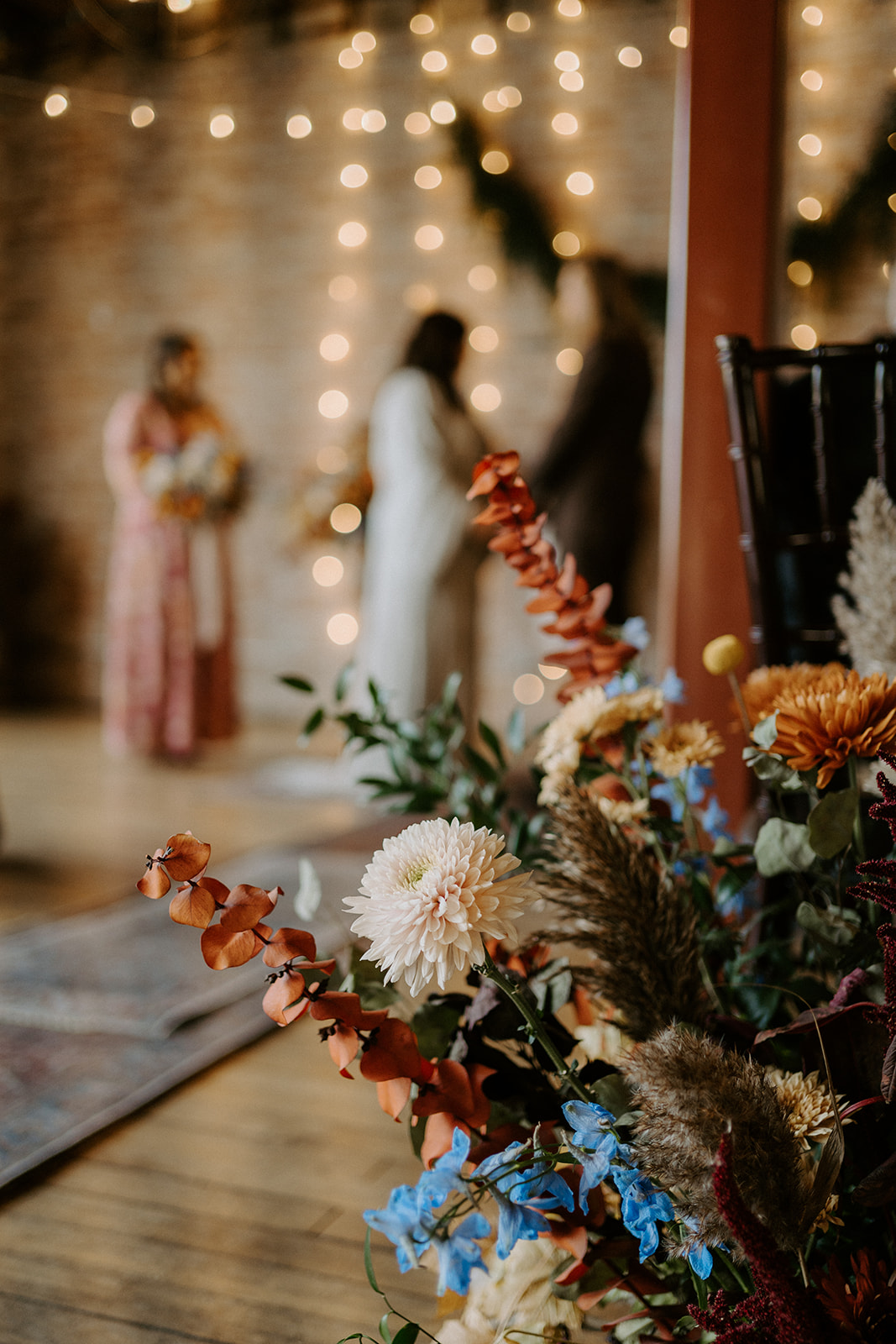 A large flower bouquet sitting on the floor with the bride and groom in the background.
