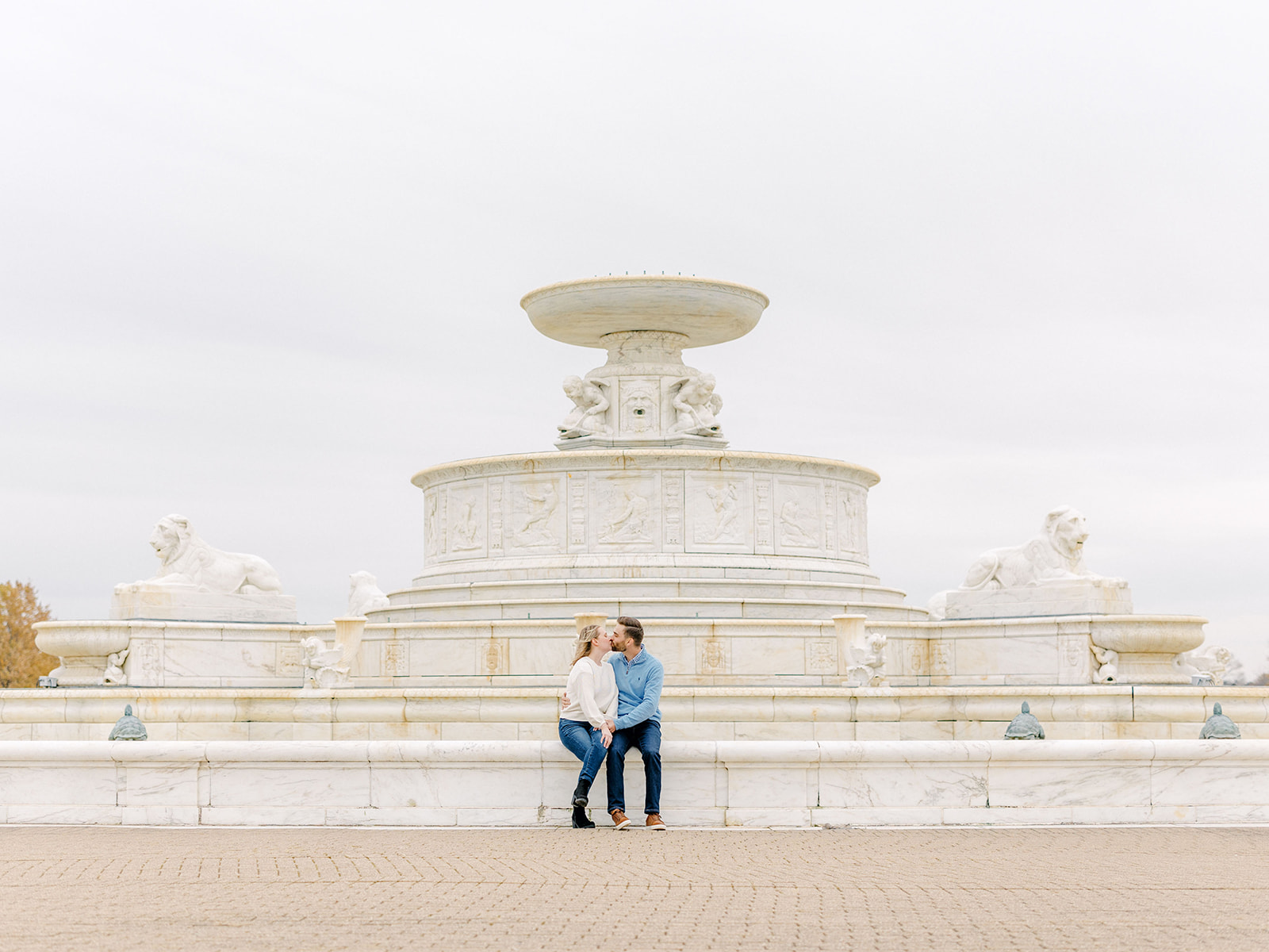 Couple sit by the fountain on Belle Isle in Detroit, Michigan for their engagement photography session.