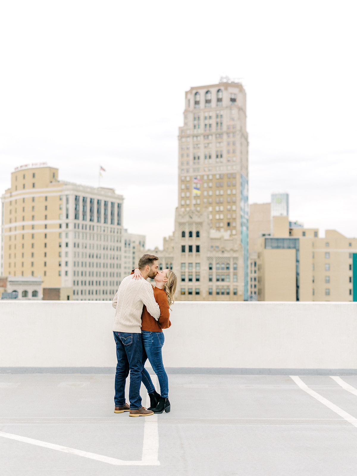 Couple kiss with Downtown Detroit, Michigan in the background of their engagement photo.