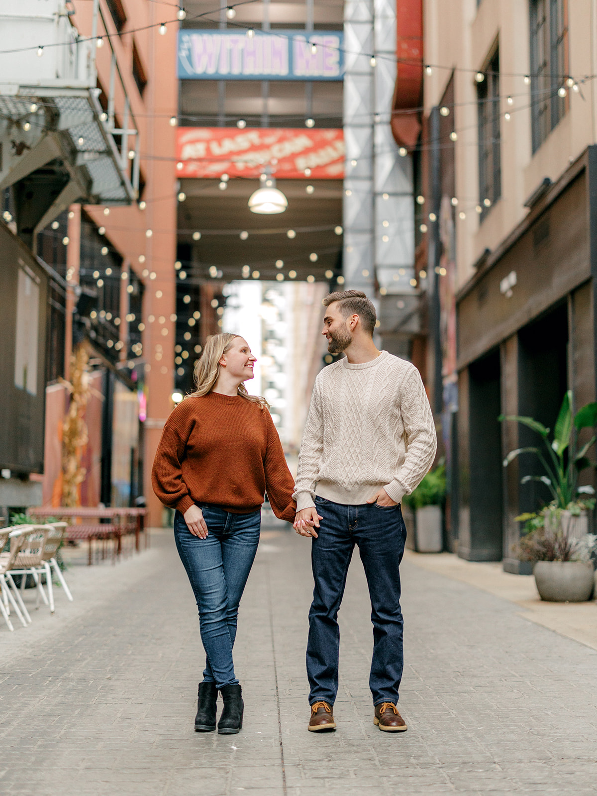 Couple holds hands with an industrial alley background for their Downtown Detroit, Michigan engagement session.