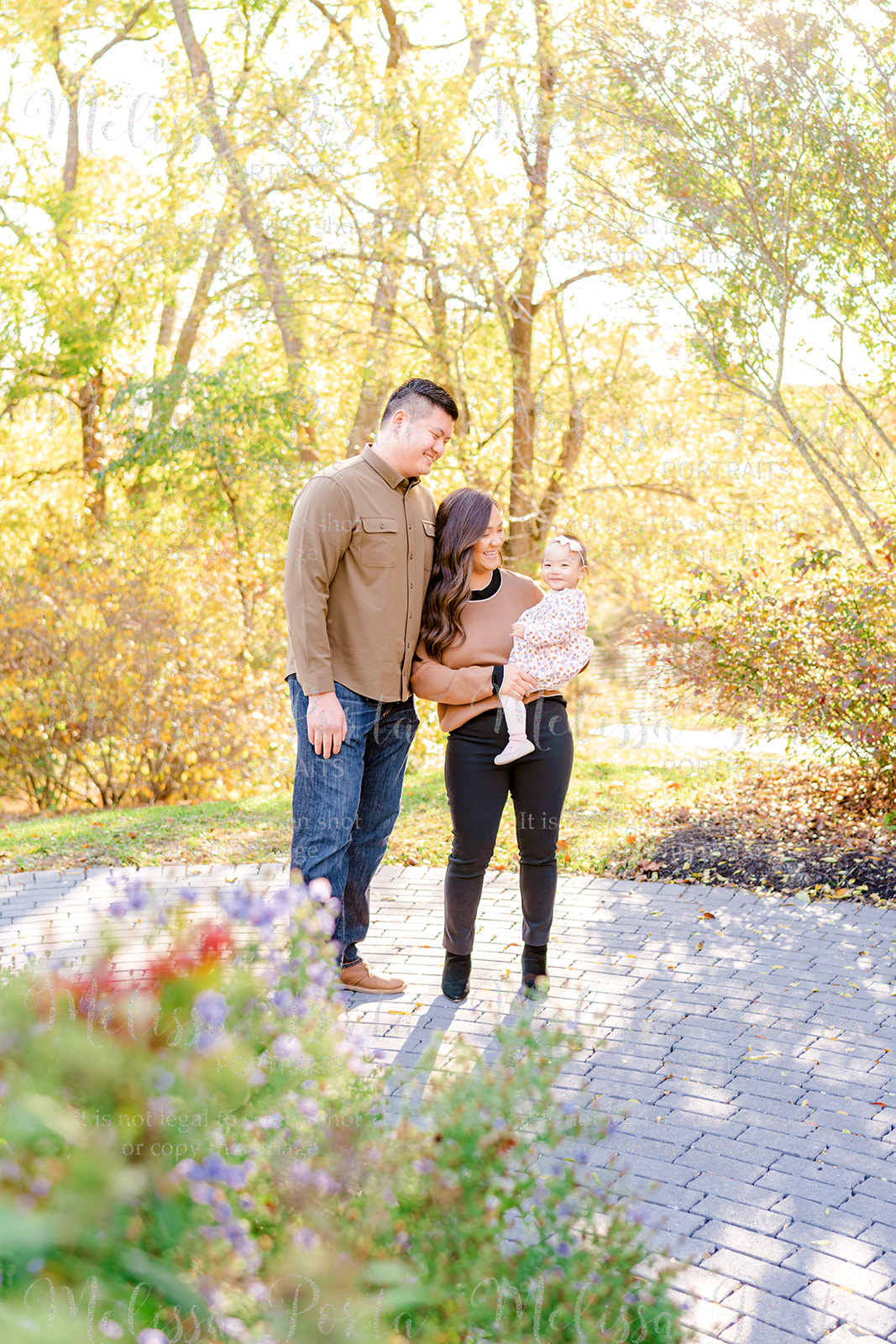 Family smiles at their baby as she smiles at the camera with fall foliage as a backdrop in Howard County, MD