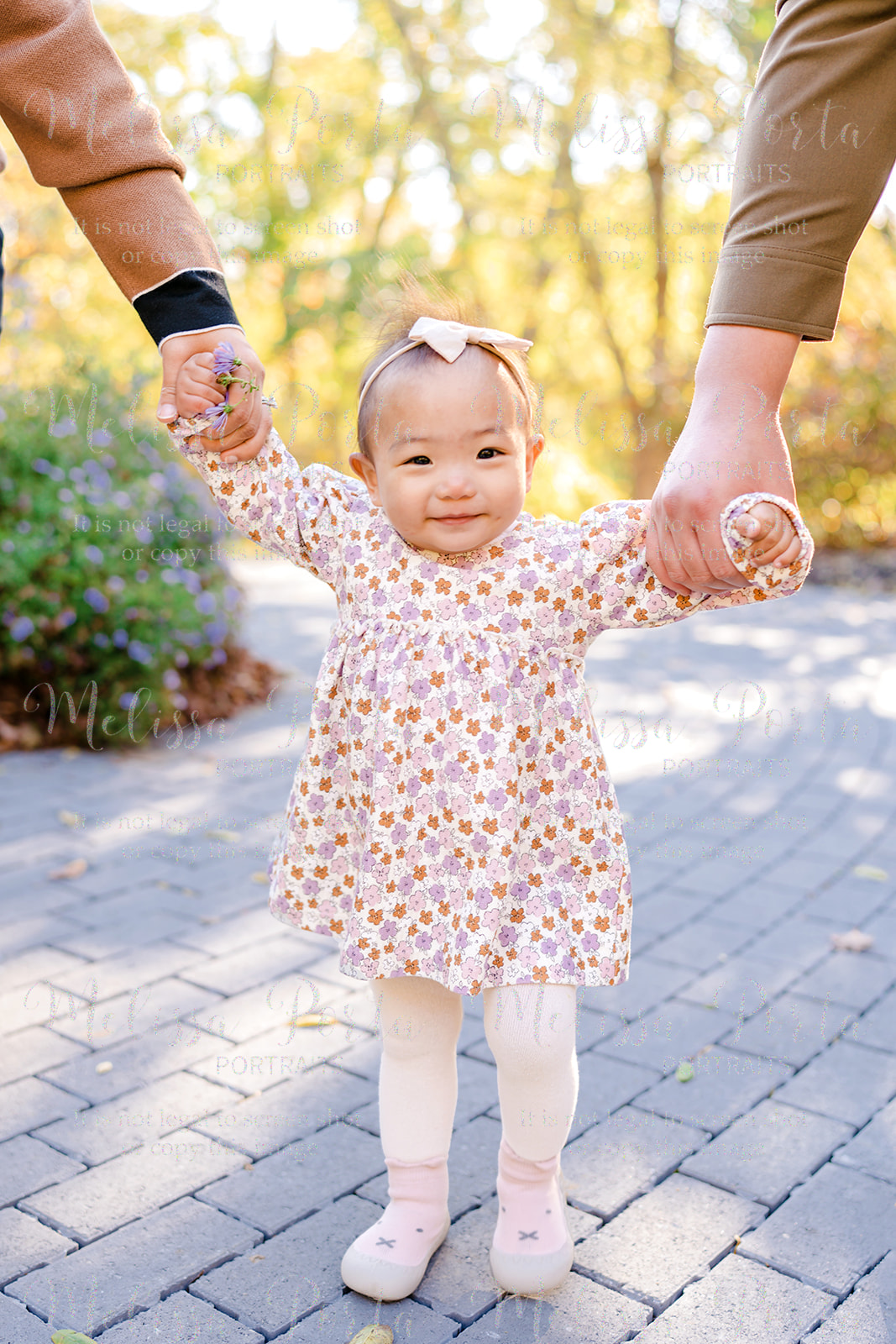 Baby holding her parents hands on a path with bright yellow trees in the background at the Conservancy in Woodstock, MD