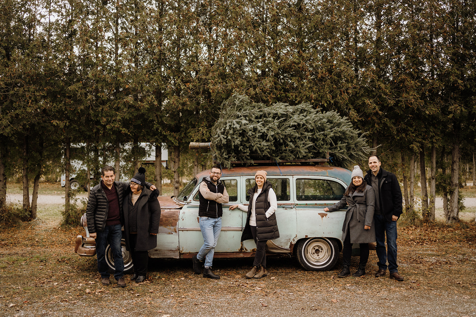 A family of six standing along a vintage looking car.