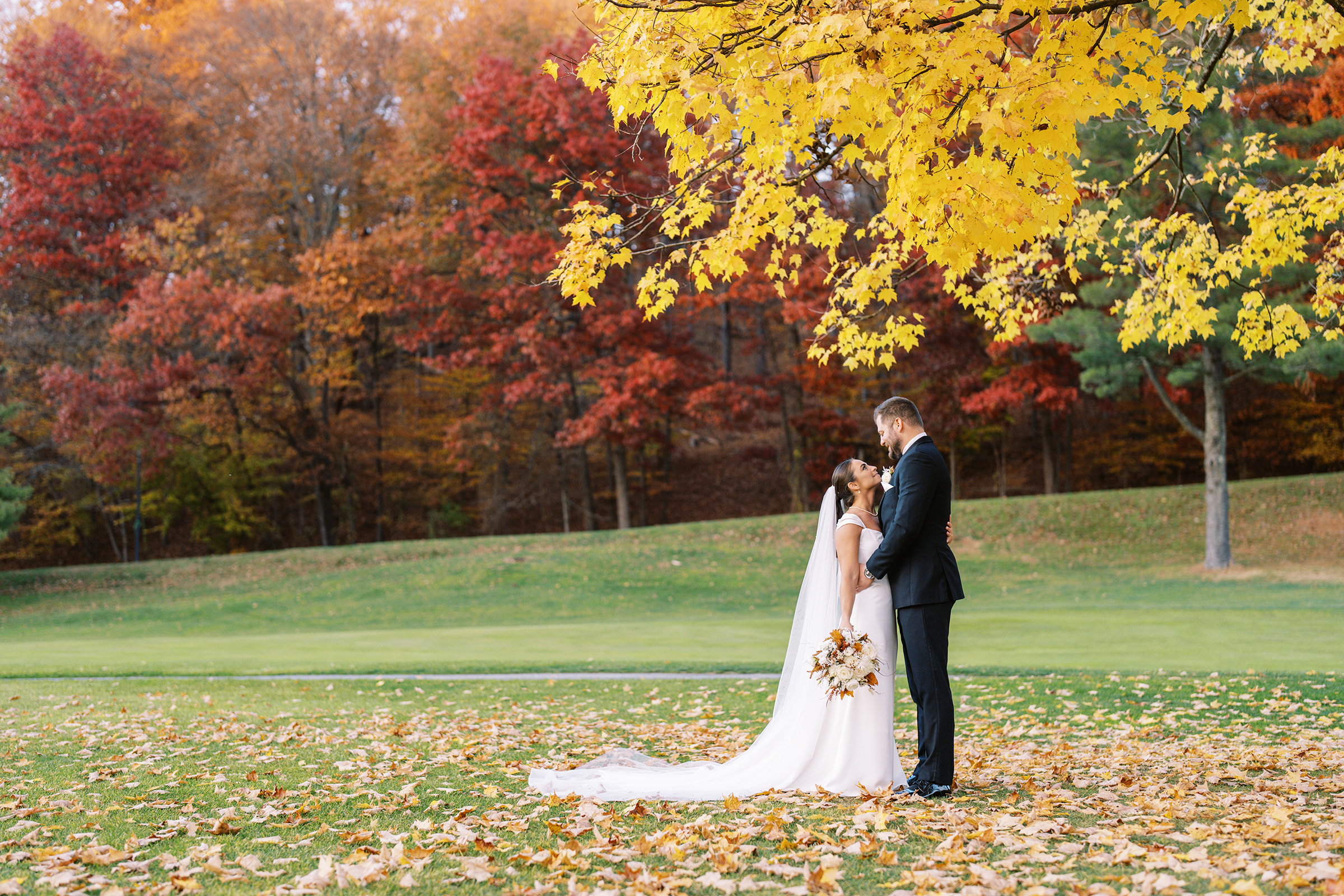 A couple just married, embracing in front of vibrant autumn leaves at thes at their wedding at Hunt Valley Country Club.