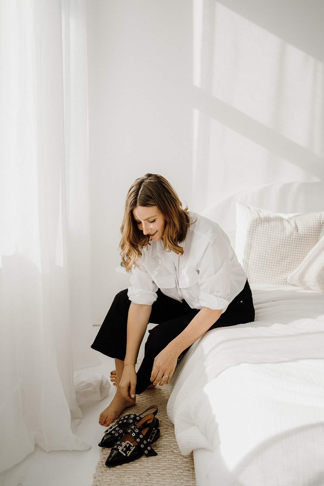 A lady sitting on the bed and reaching for her shoes.