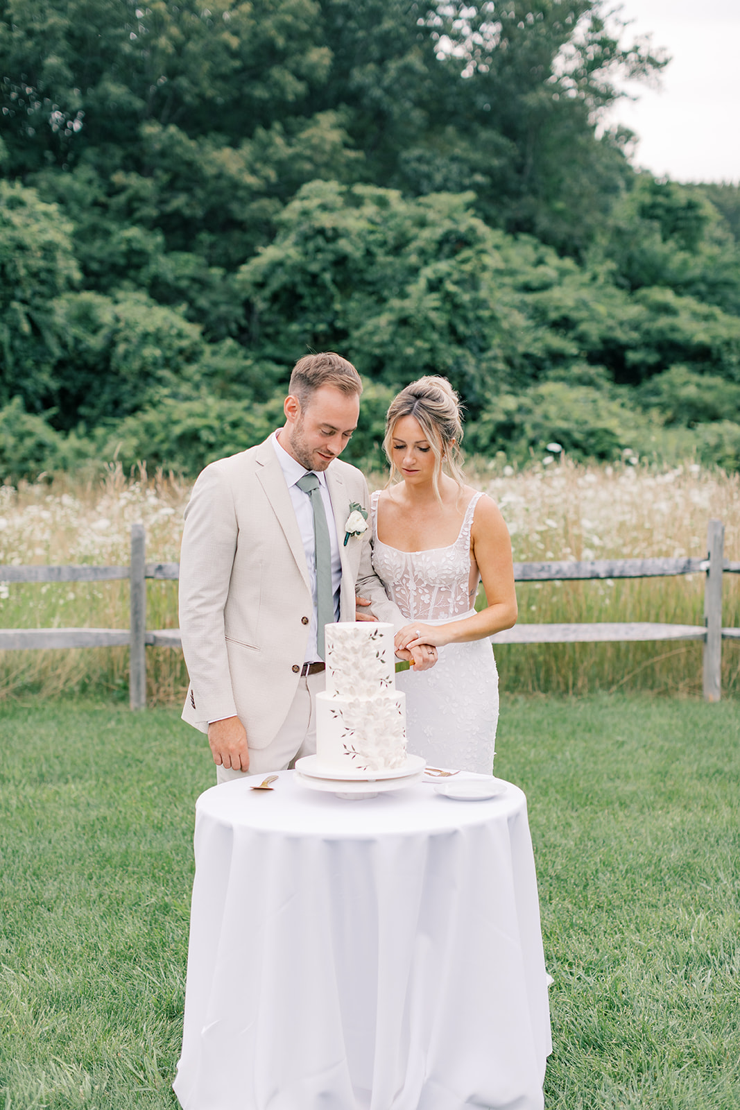 bride and groom cutting custom floral cake with field in the background