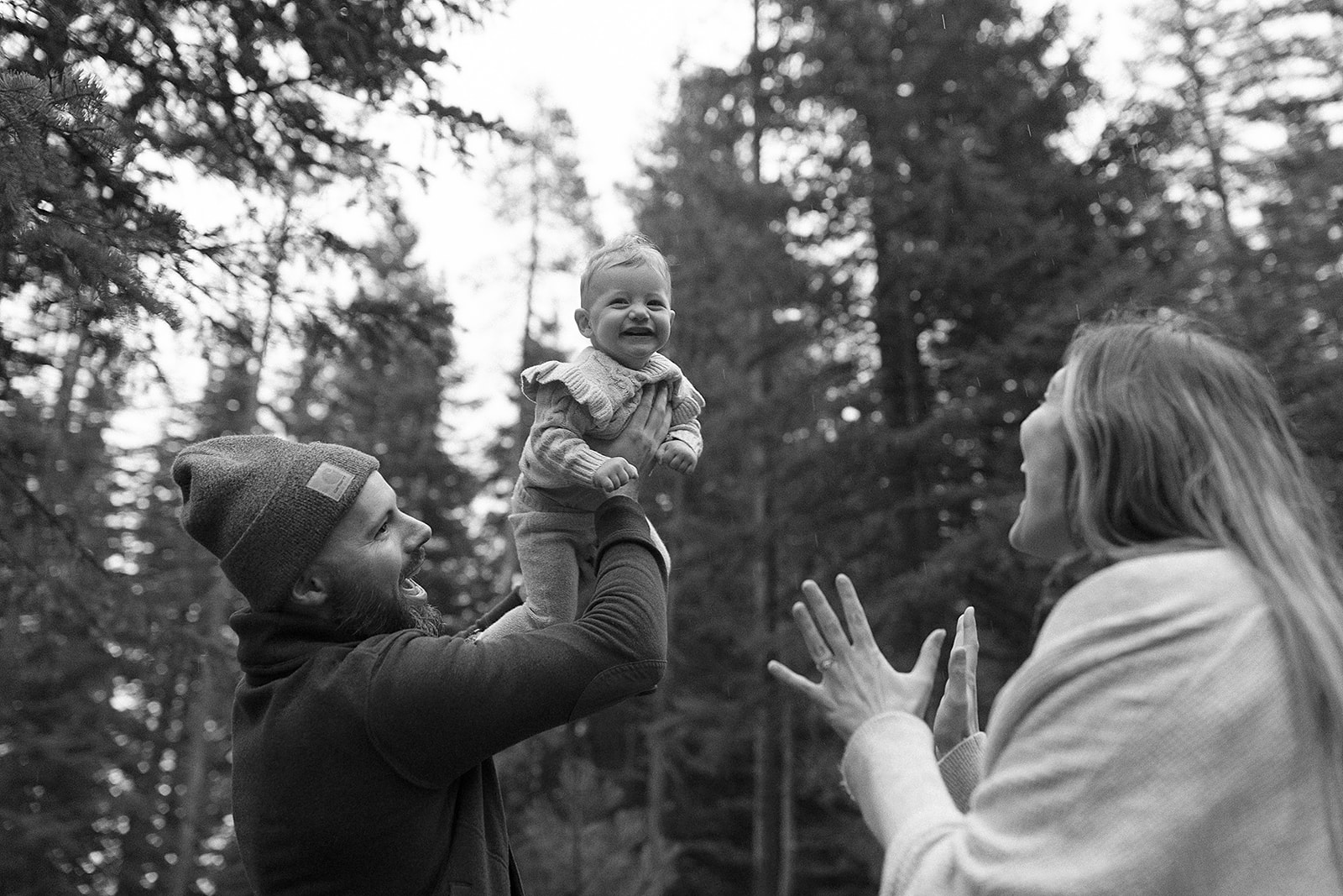 parents playing with their child, with dad holding daughter up in the air and baby laughing at the camera