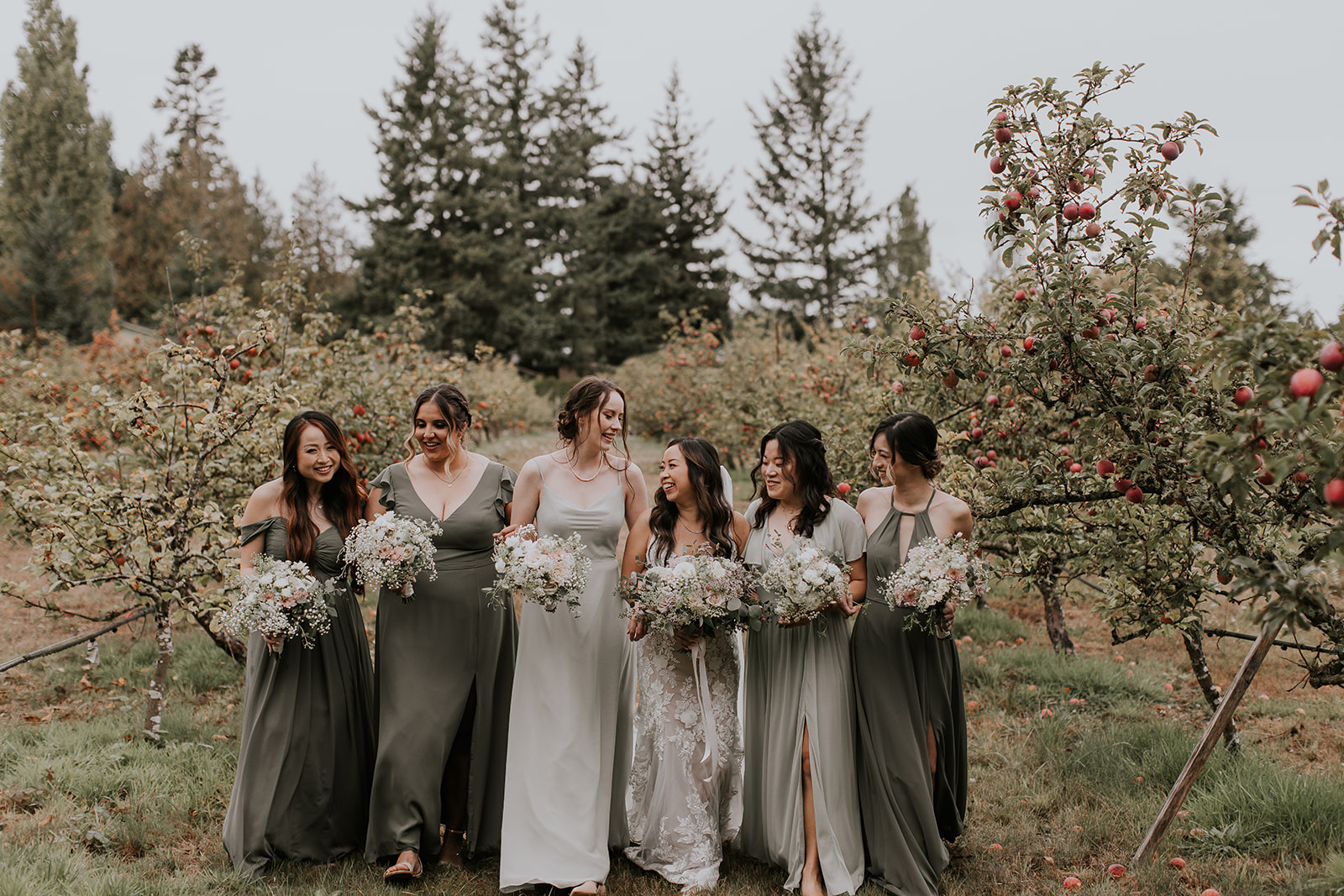 a bride and four bridesmaids laugh and  walk through an orchard at Sea Cider Farm in Sannichton, BC