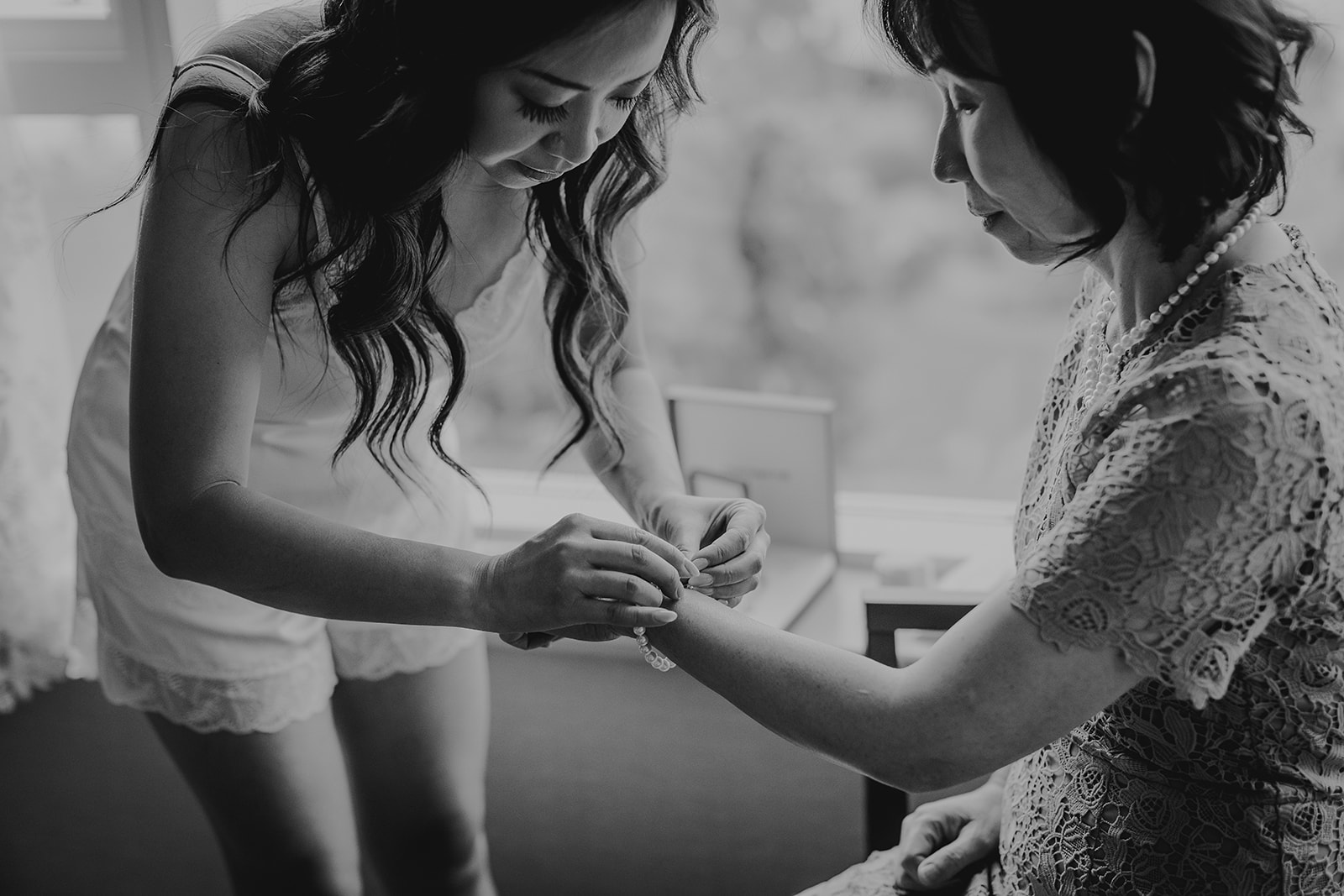 a bride in pyjamas helps her mother put on a bracelet 