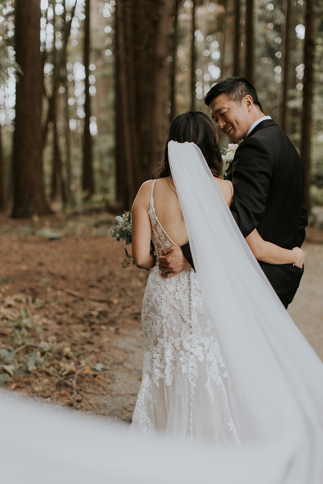 a groom and bride walk away through a forest 