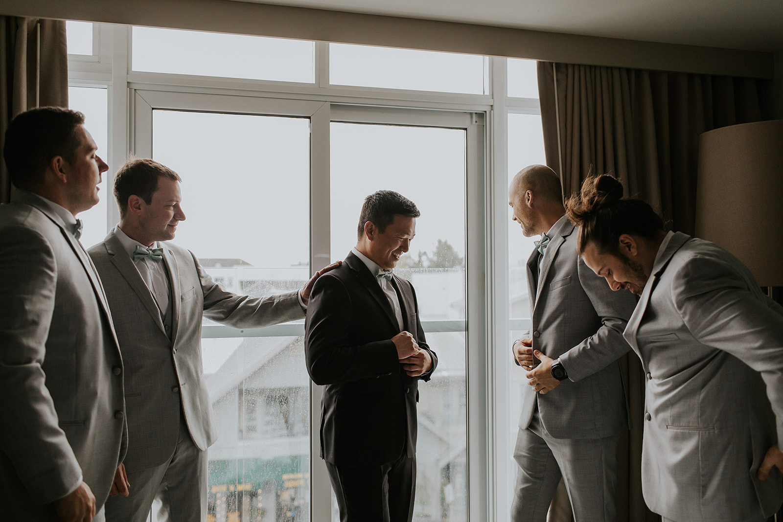 a groom and his groomsmen laugh in front of a window at the sidney pier hotel