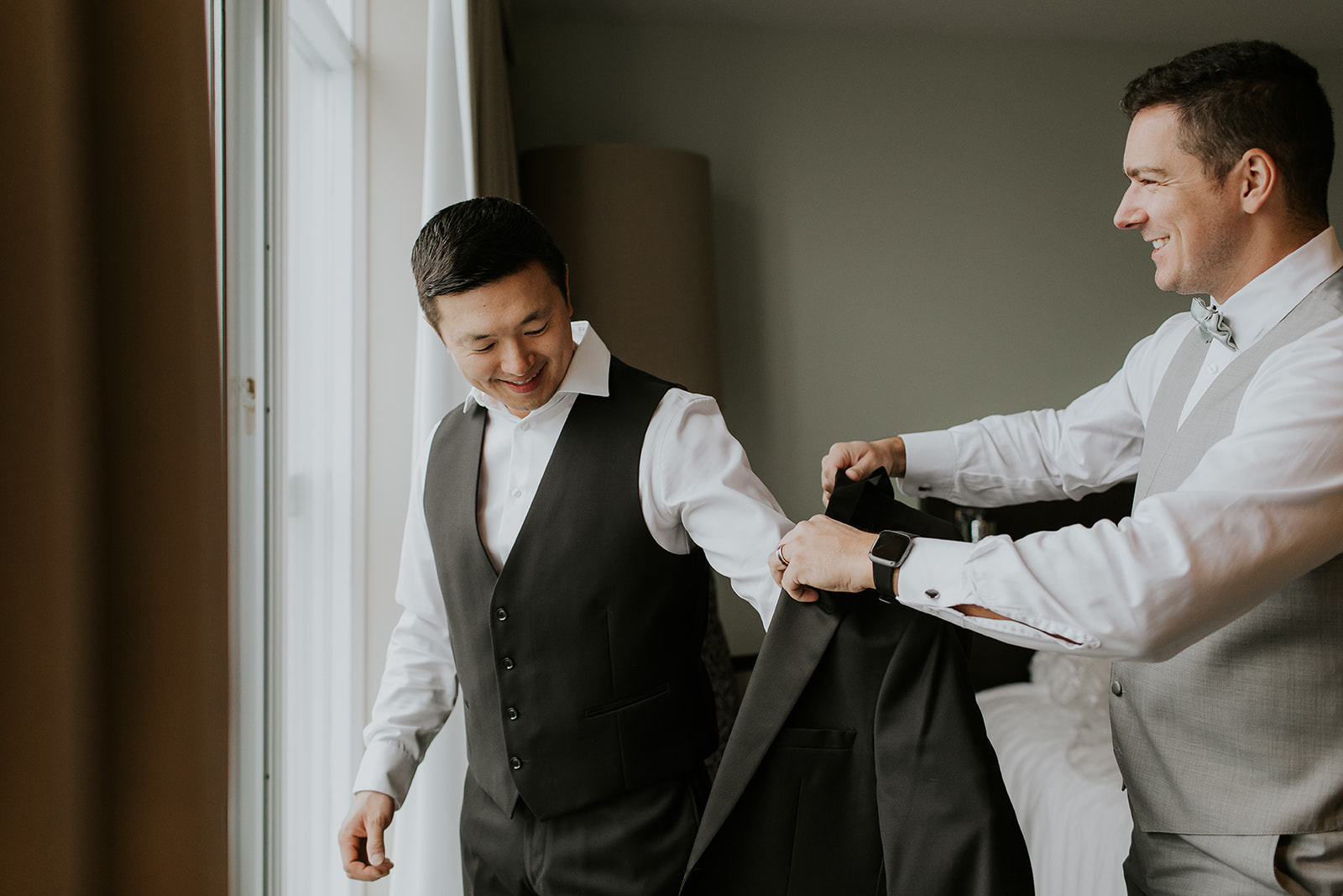 a groomsmen helps a groom get his suit jacket on