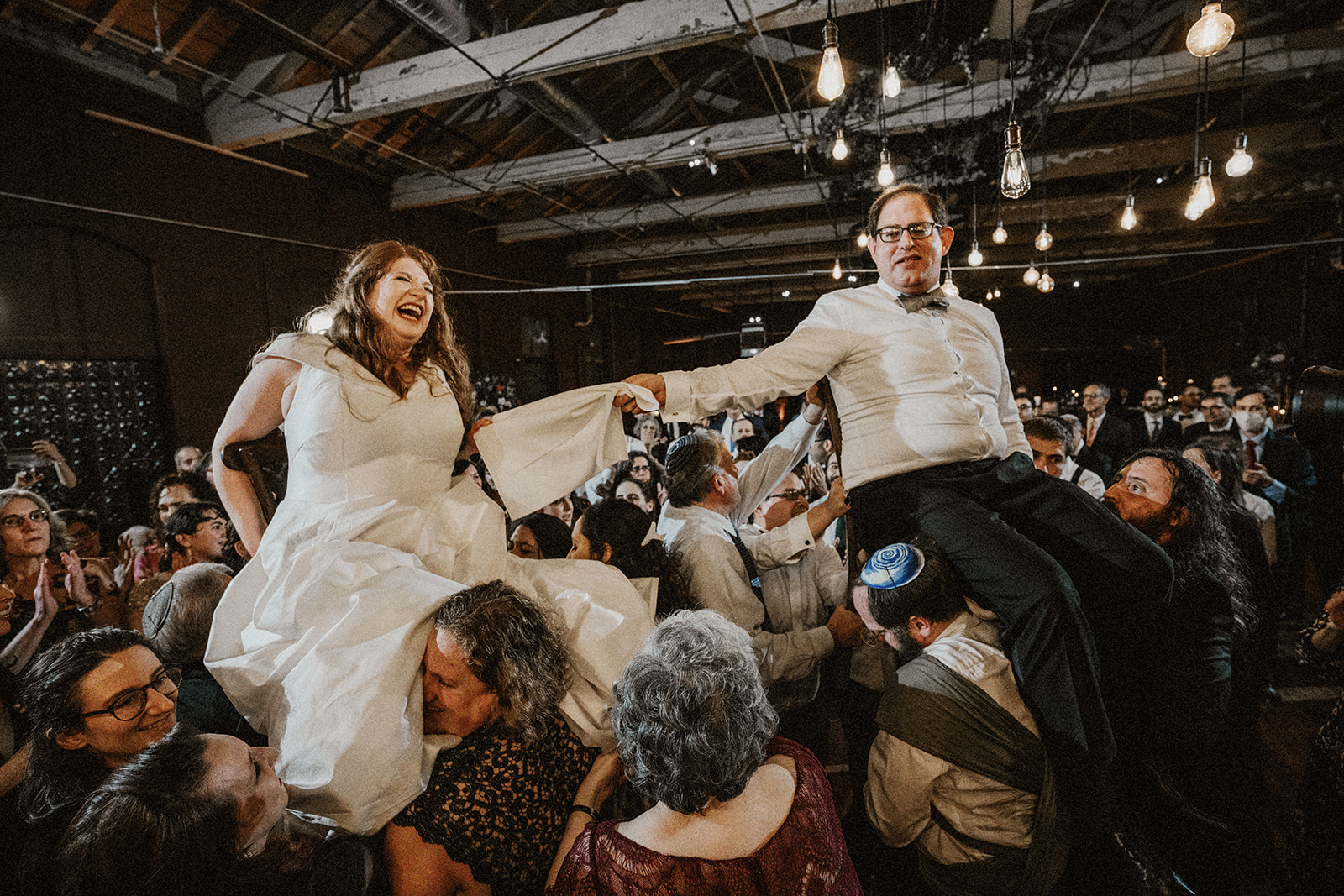 bride and groom raised by chair in horah during orthodox jewish wedding reception
