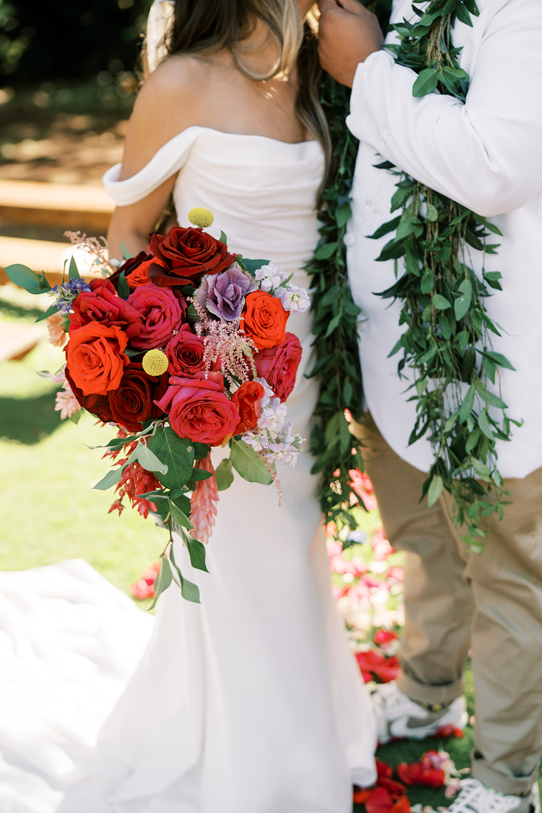 A bride holding a bouquet of red roses with a groom wearing a garland durig their Hawaiian Wedding in Kauai