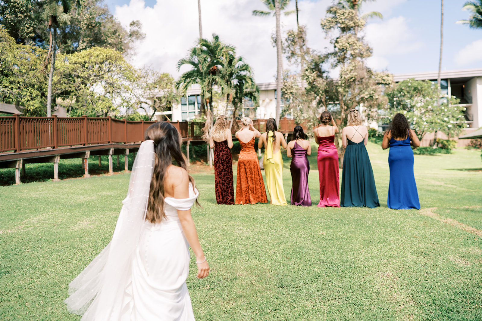 A bride approaching a group of bridesmaids dressed in colorful gowns, all standing outdoors on Smiths Tropical Paradise