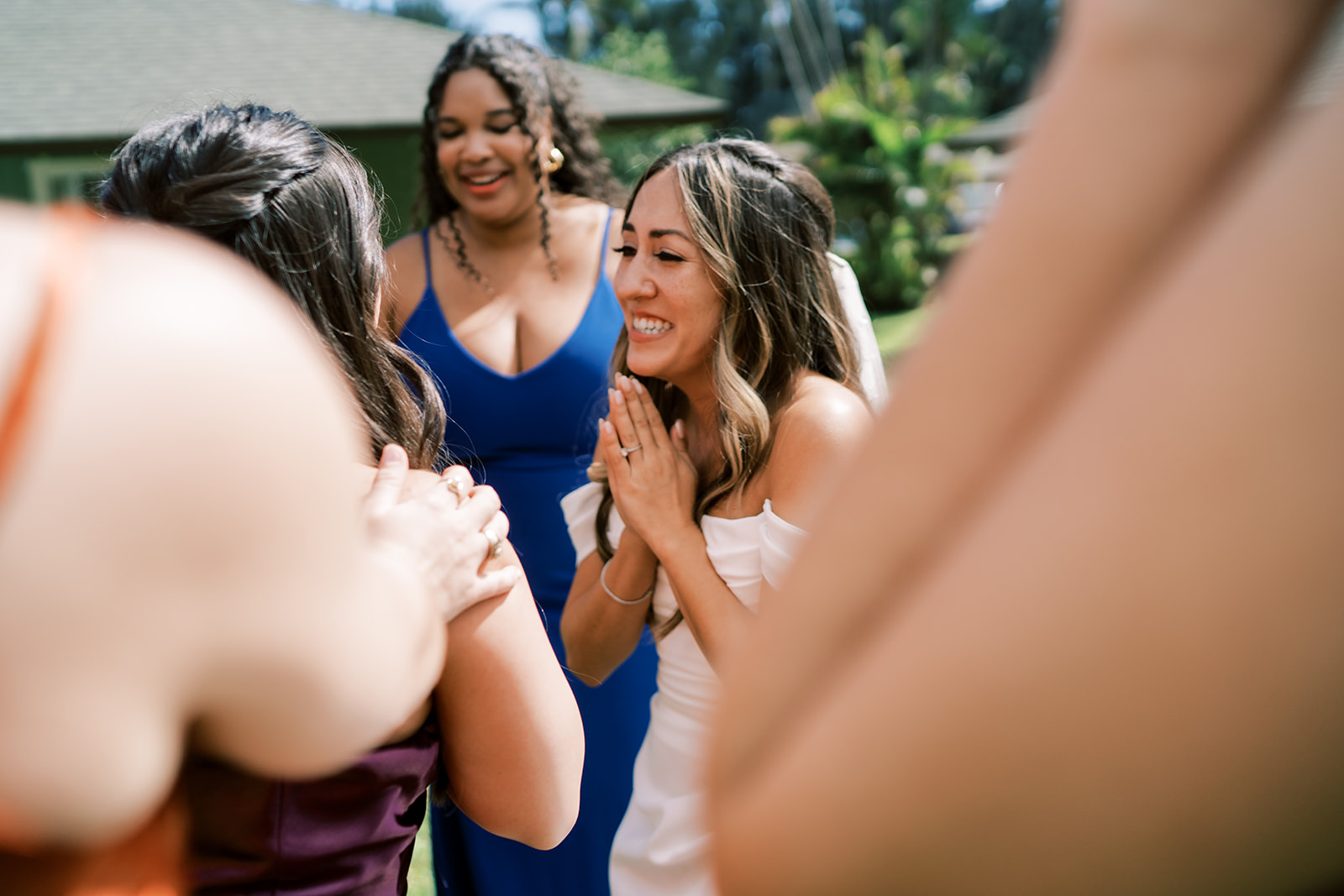 A joyful bride clasping her hands together while interacting with guests, with a bridesmaid smiling in the background.