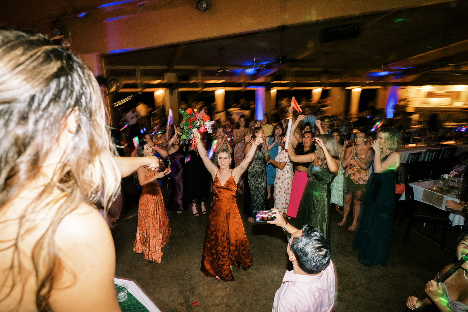 A bride tossing her bouquet to a crowd of excited guests at a wedding reception in Smiths Tropical Paradise and Luau