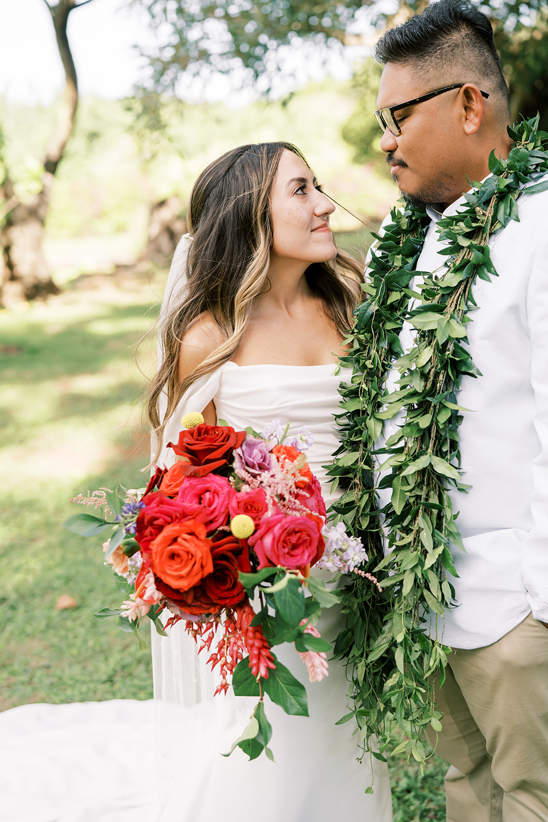 A bride holding a bouquet gazes at a groom wearing a lei on their Hawaiian Wedding at the Smiths Tropical Paradise