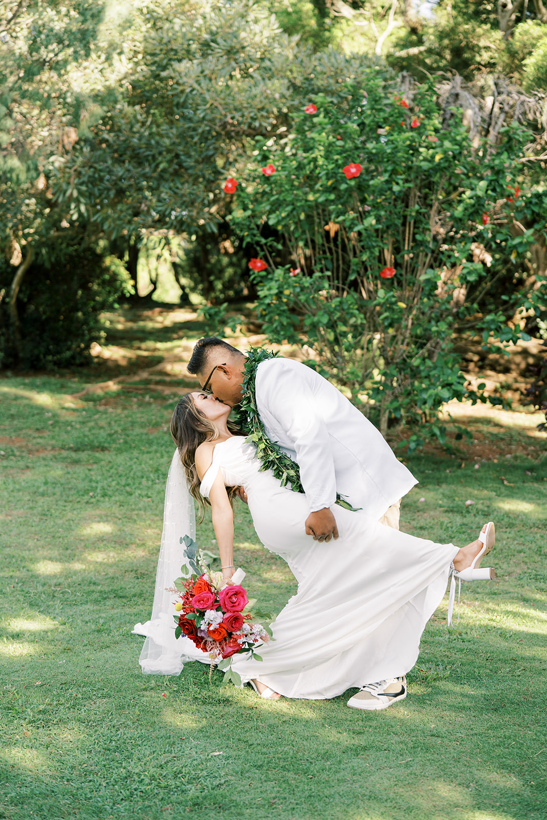 A couple in wedding attire sharing a kiss in a garden setting in Kauai.