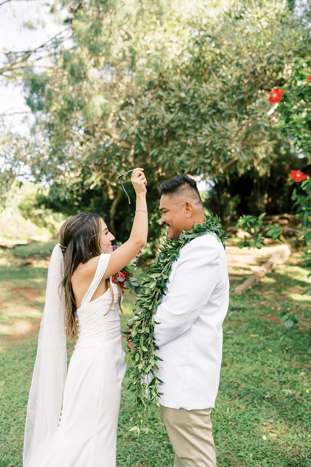 A bride placing a floral garland over the head of a smiling groom during their Hawaiian Wedding