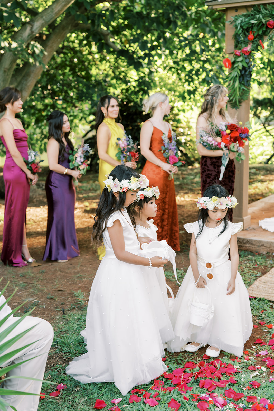 Bridesmaids and flower girls at a Hawaiian wedding ceremony, standing amidst scattered petals.
