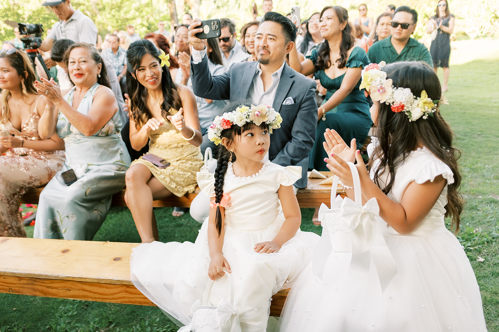 Two flower girls in white dresses with floral headpieces are interacting at Hawaiian wedding captured by Megan Moura