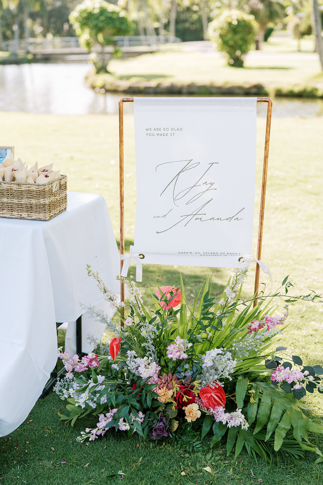 Welcome sign at an outdoor Hawaiian Wedding with a floral arrangement.