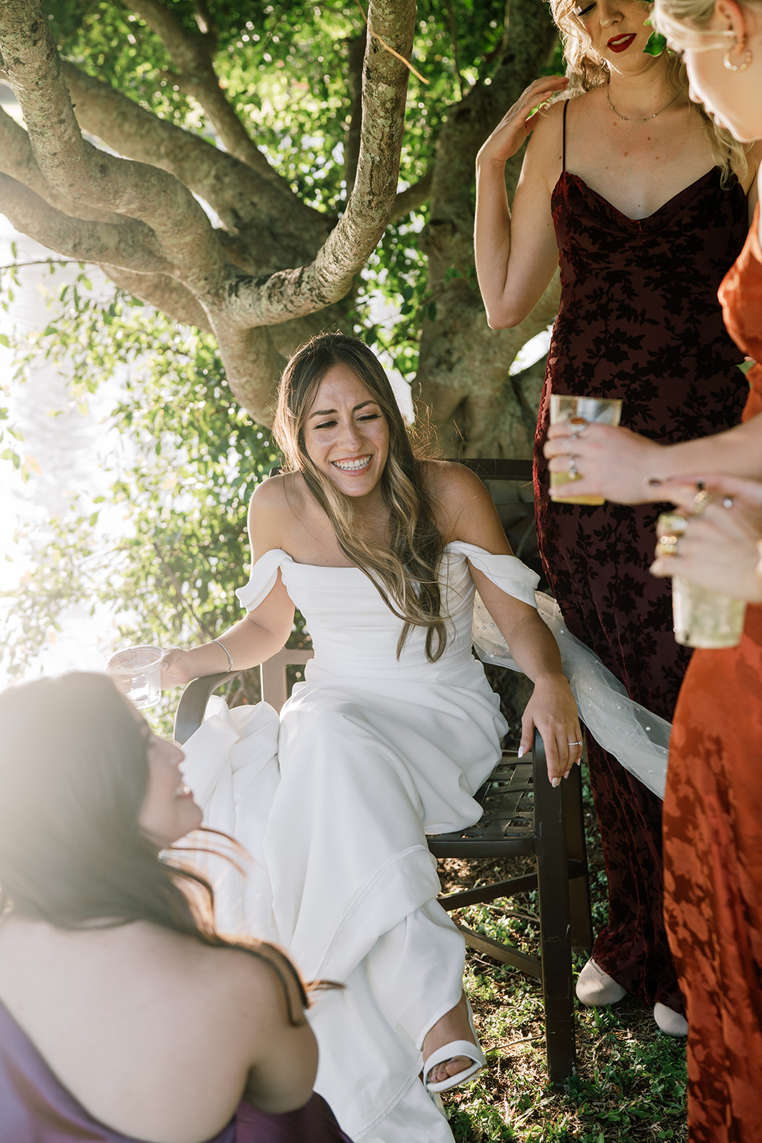 A bride in a white dress laughing with her bridesmaids in a garden setting during a Hawaiian Wedding Reception