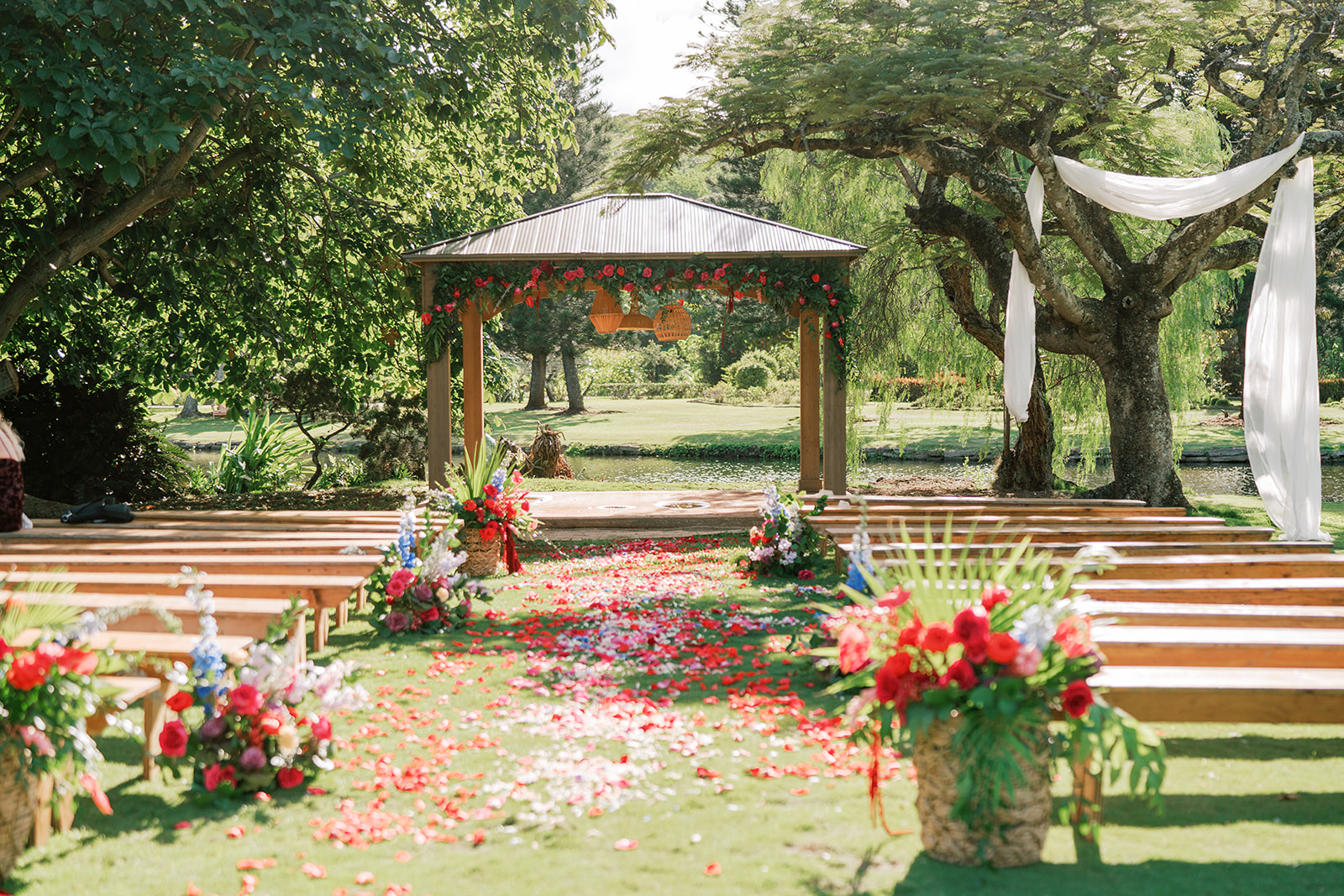 Outdoor Hawaiian wedding setup with a floral-decorated gazebo and petal-strewn aisle in a garden setting in Kauai