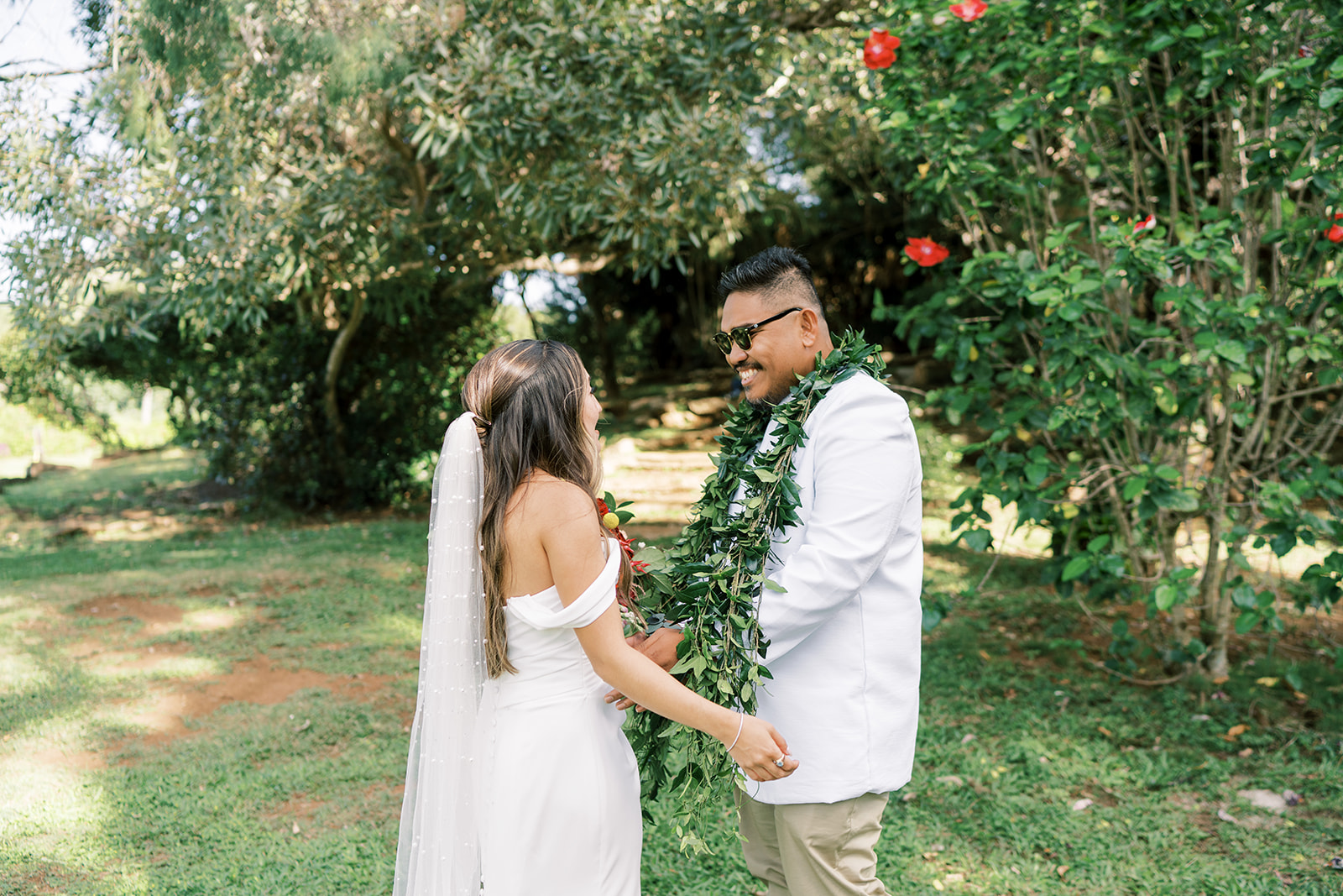 A newlywed couple holding hands and smiling at each other in a garden setting captured by Megan Moura