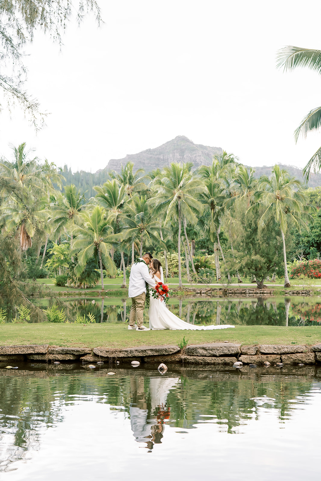 Couple embracing at a tropical lakeside with palm trees and mountain in the background taken by Megan Moura