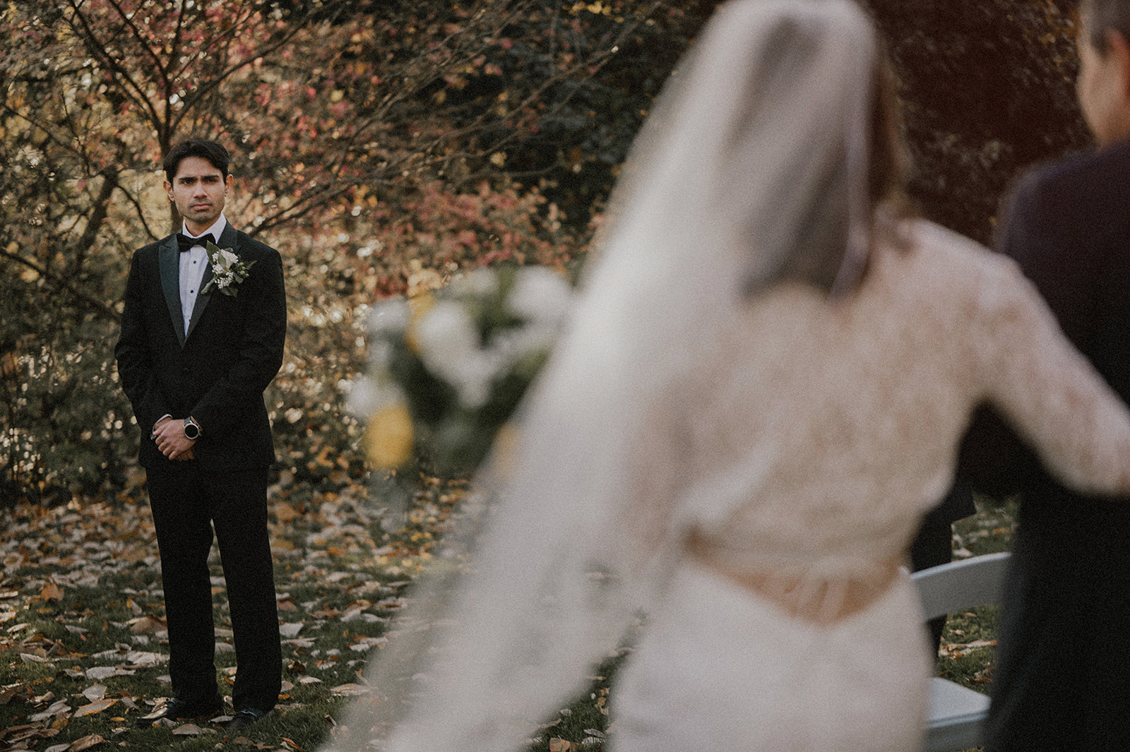 back view of bride walking down the aisle with groom looking at her in background surrounded by fall foliage