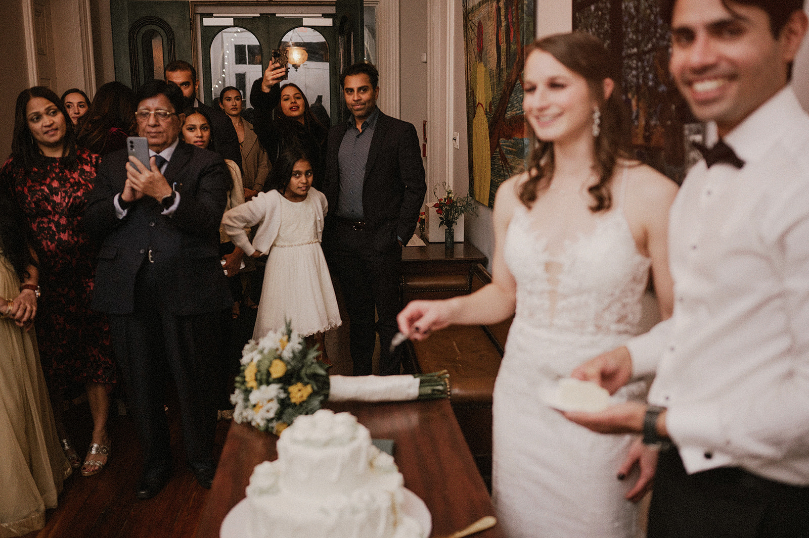 bride and groom cutting wedding cake with family and friends looking and clapping