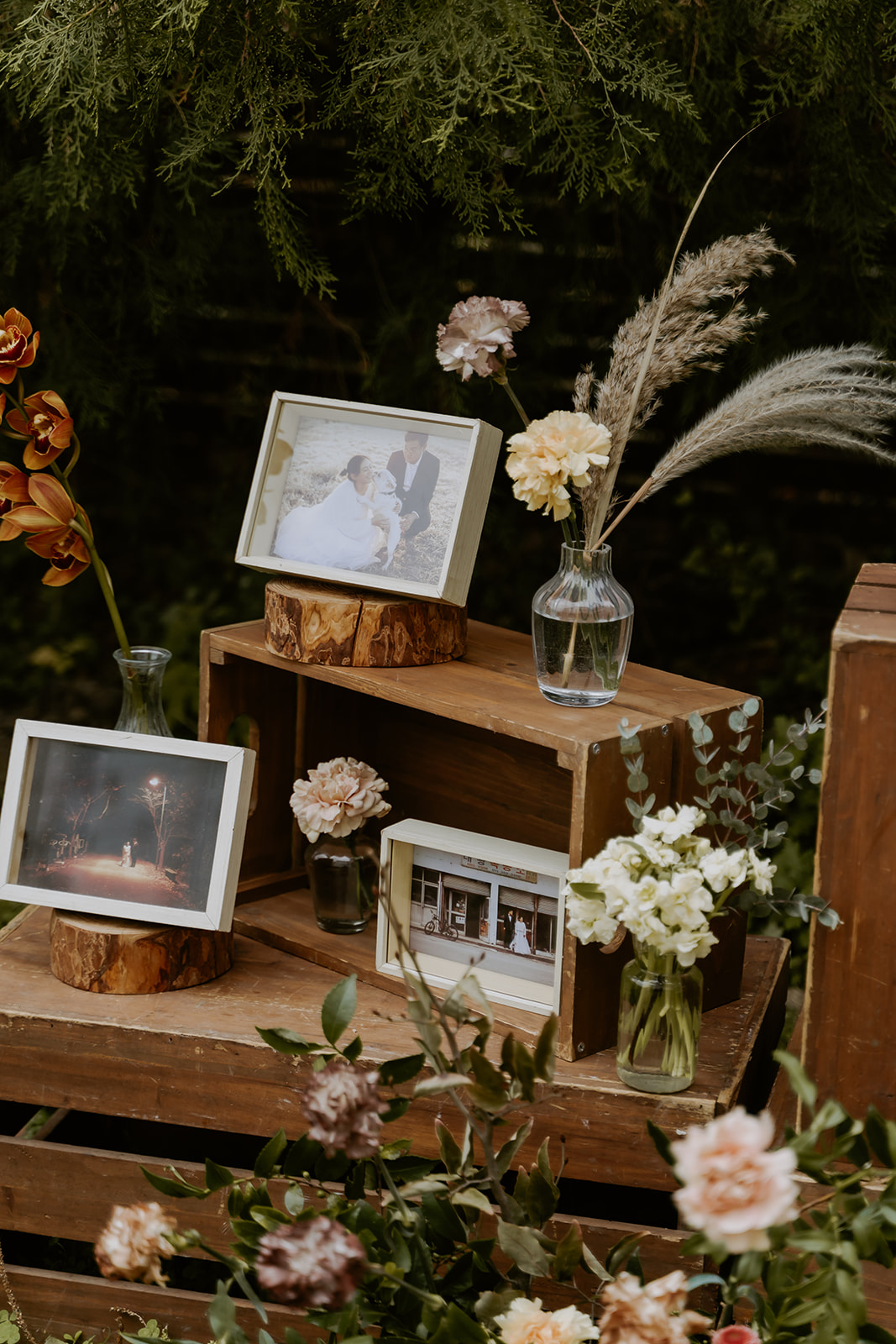 A framed wedding photo placed atop a rustic wooden pedestal surrounded by an assortment of flowers and plants.