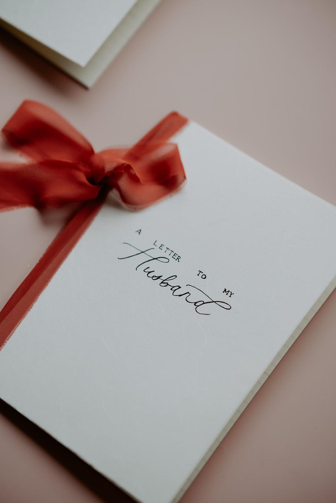 A letter with the handwritten words "a letter to my husband" beside a white gift box with a red ribbon.