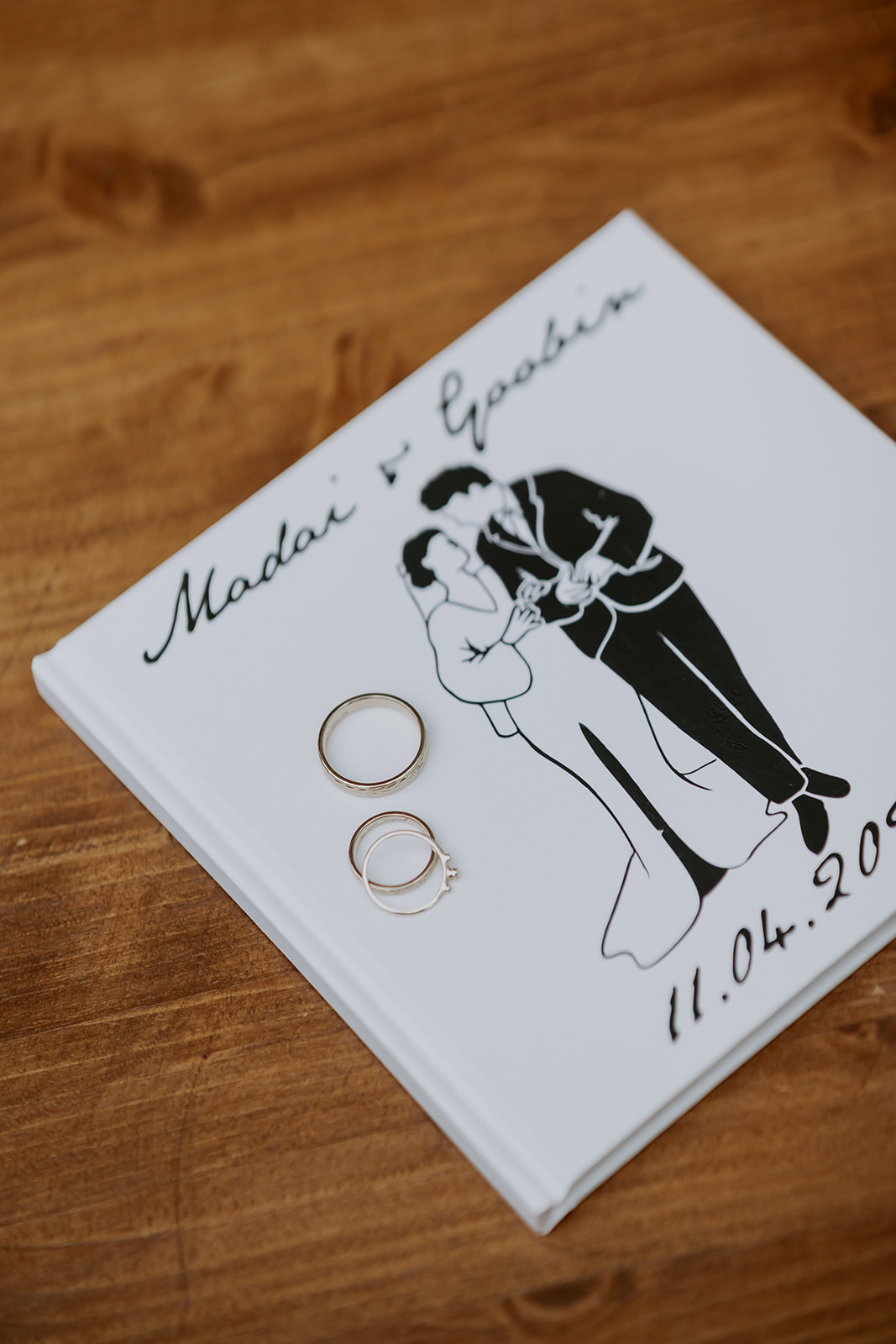 White wedding album featuring a black illustration of a couple dancing, with two rings on top and a date: 11.04.2023.