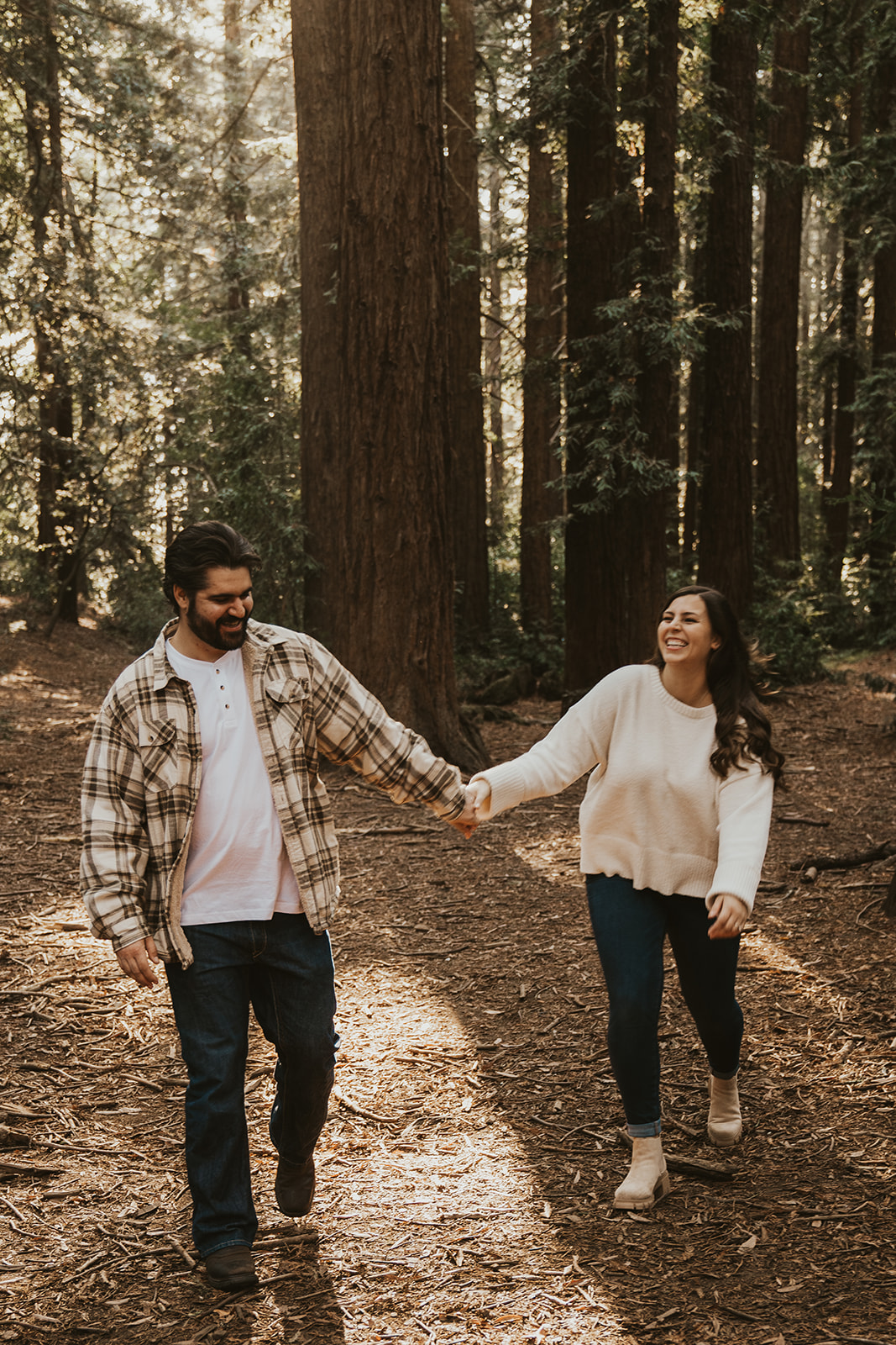 Engaged couple laughing and holding hands in the Oakland Redwoods