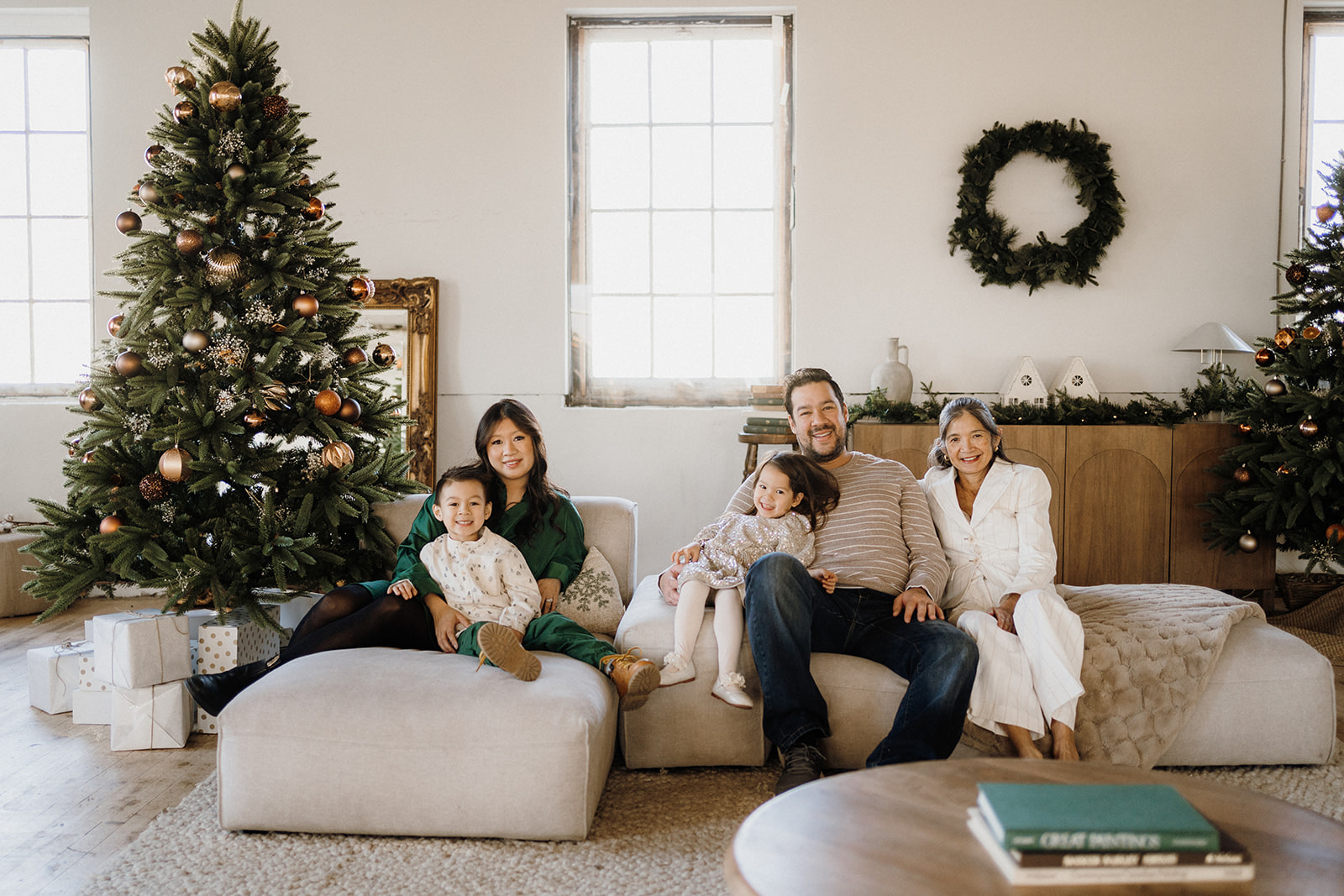 A family of five sitting on the couch beside the Christmas Tree.