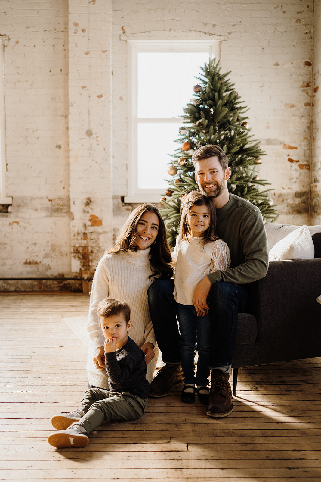 A family of four sitting in front of a Christmas Tree inside.