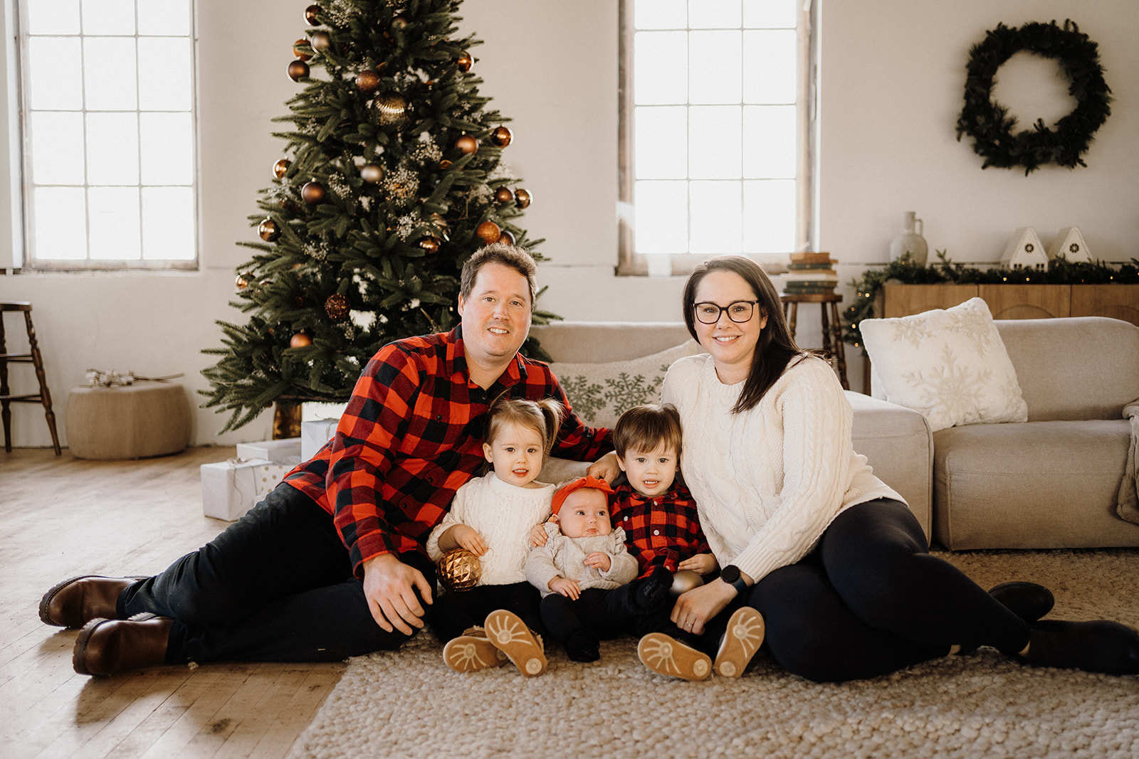 A family of five sitting on the ground in front of a Christmas Tree.