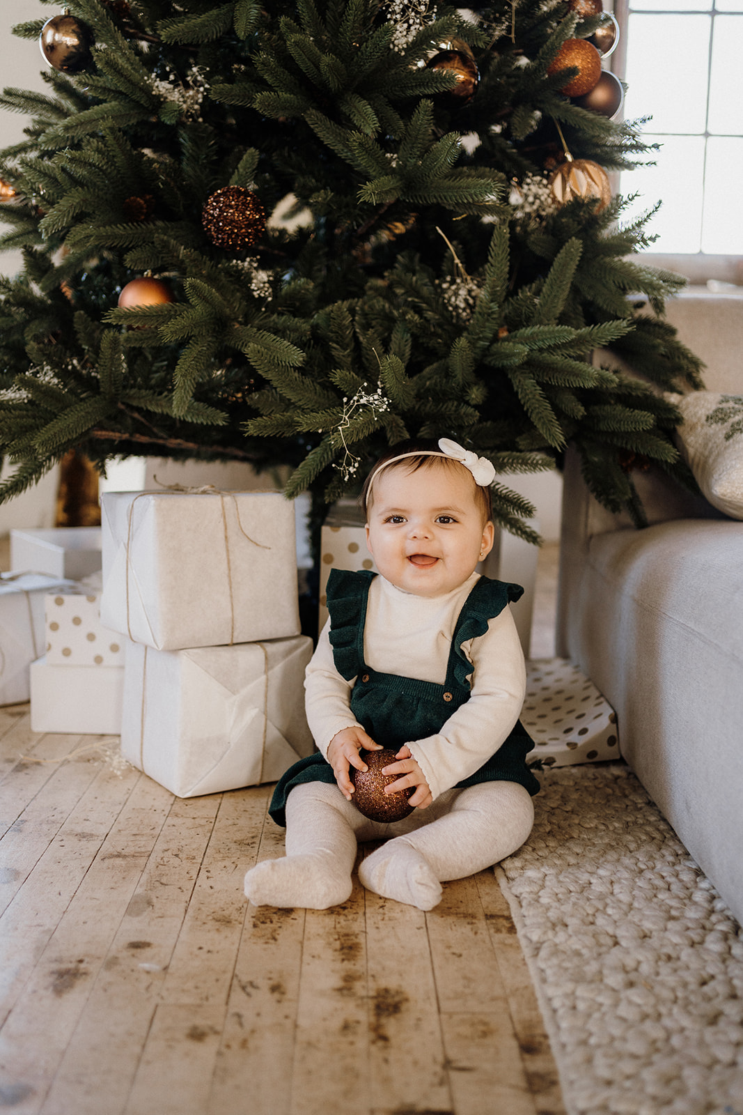 A child sitting on the ground in front of the Christmas Tree.