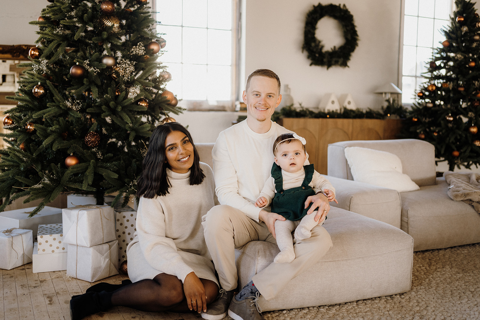 A family of three sitting inside in front of a Christmas Tree.